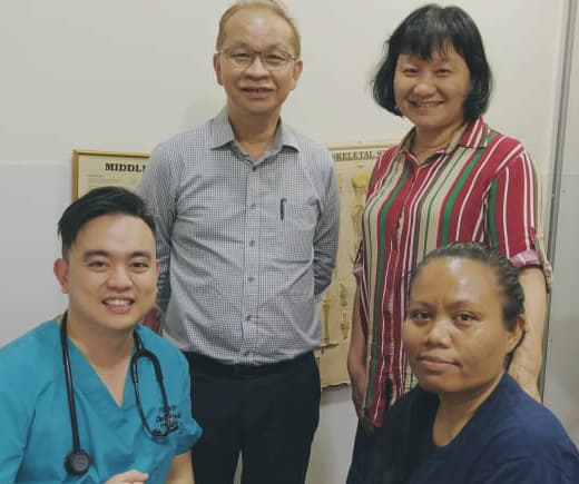 诊所职员与病人在诊症室内合影，身旁挂着一幅人体解剖图。