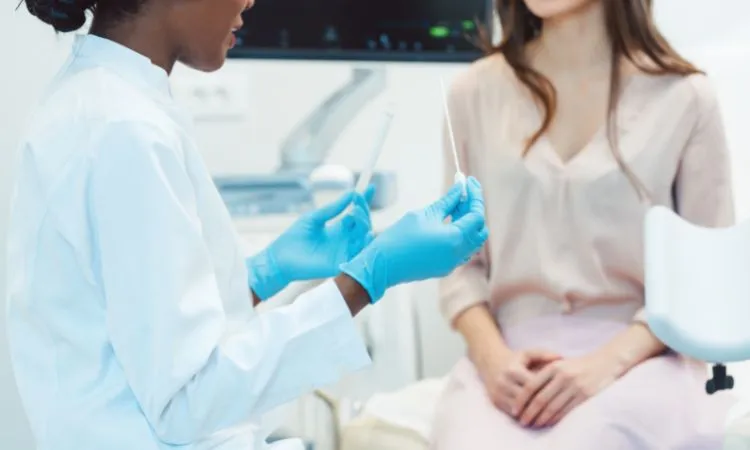 A clinician in gloves holding a swab while talking to a seated patient in an examination room