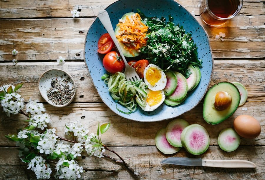 Overhead view of a salad bowl with boiled egg, tomato, avocado and greens on a rustic wooden table