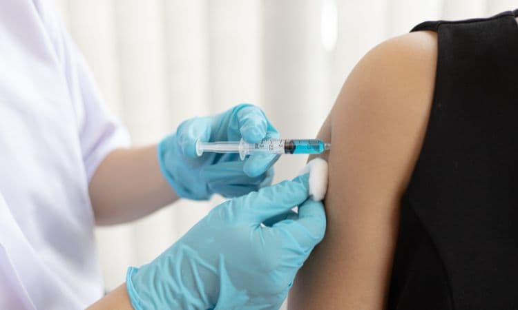 A gloved healthcare worker injecting a syringe into a woman's upper arm