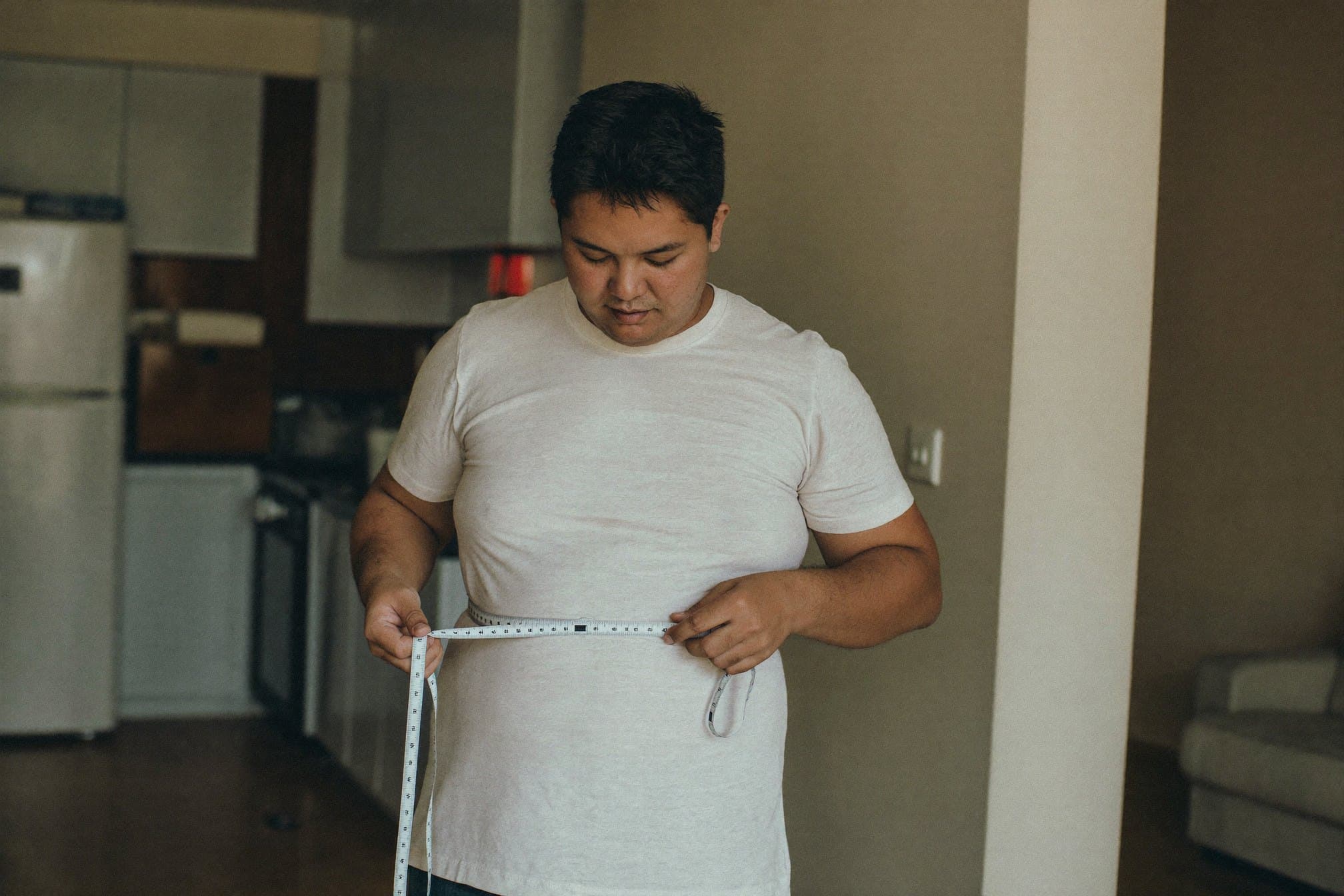 A man measuring his waist with a tape measure at home