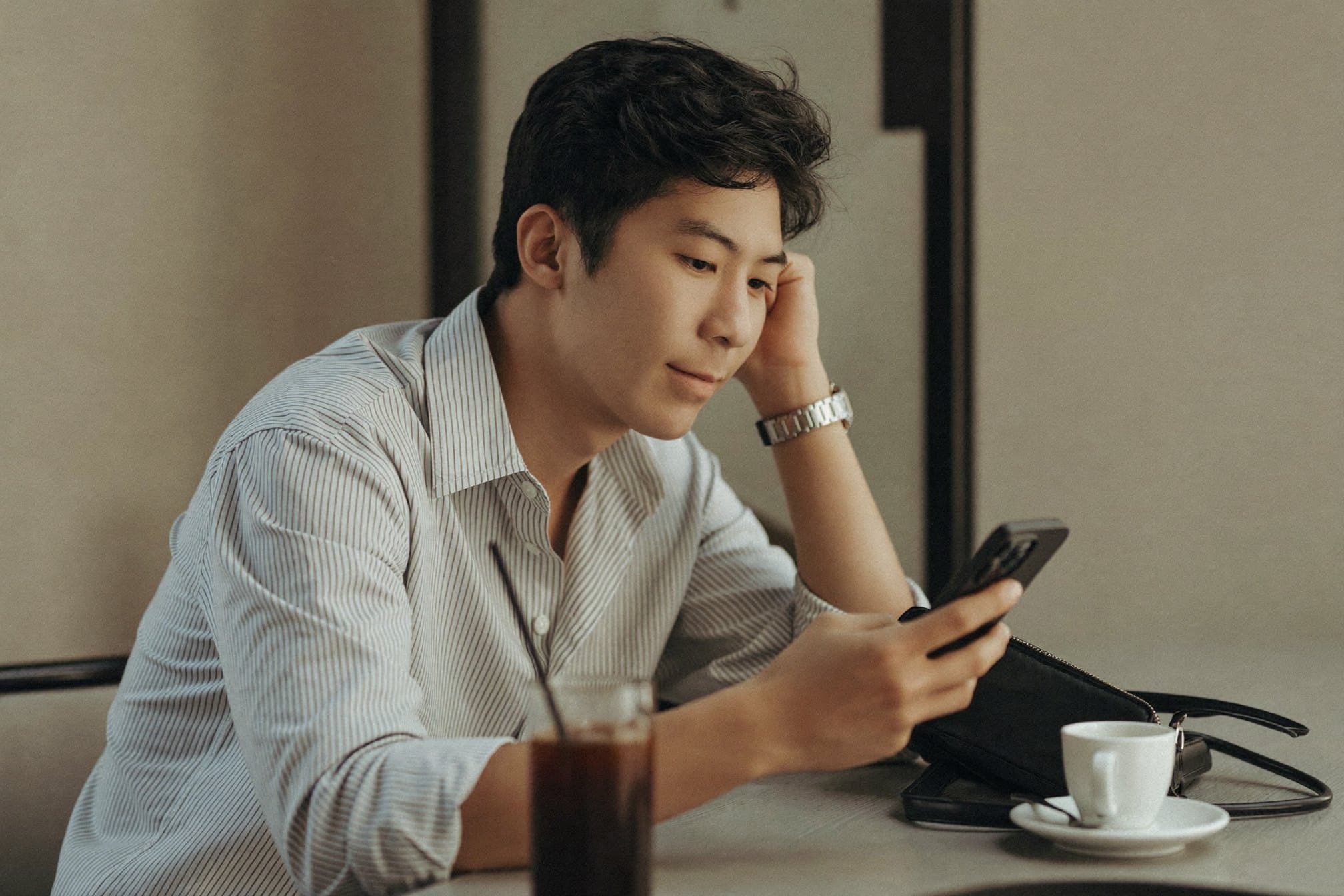 A young man reading a message on his phone at a cafe table