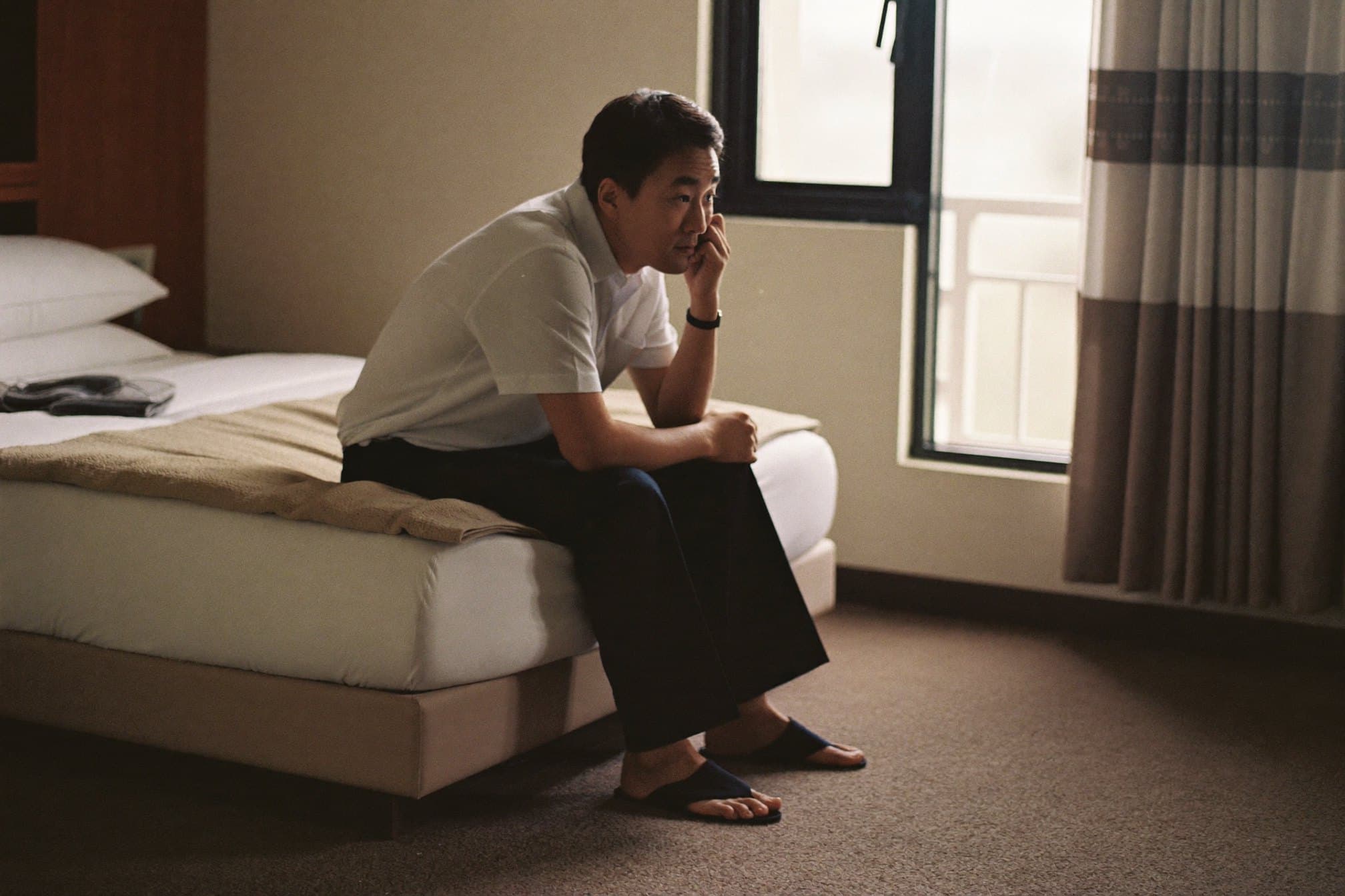 A man sitting on the edge of his bed in the morning, deep in thought