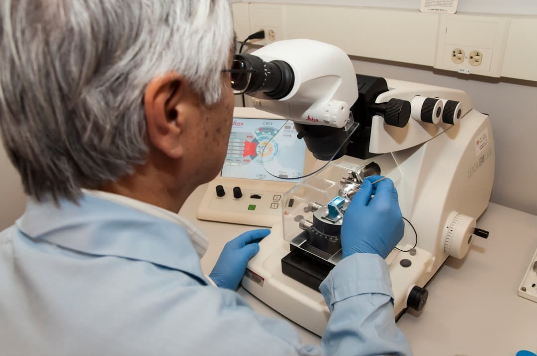 A grey-haired laboratory scientist loading a specimen block into a microtome beside a microscope.
