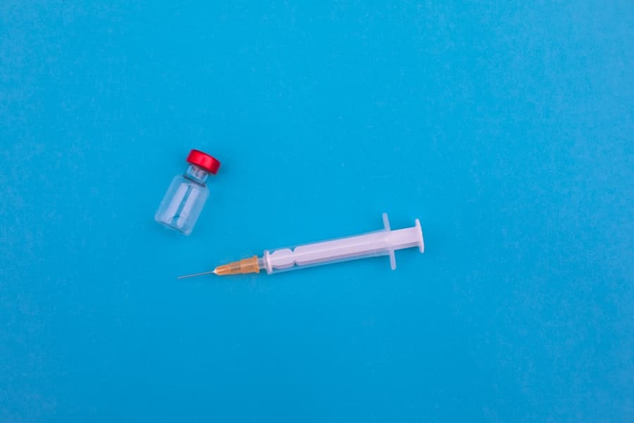 An empty syringe and a small red-capped glass vial lying on a blue surface